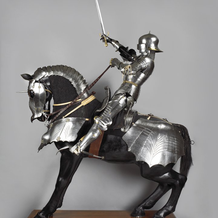 Full length photograph of a medieval knight on an armoured horse from the left