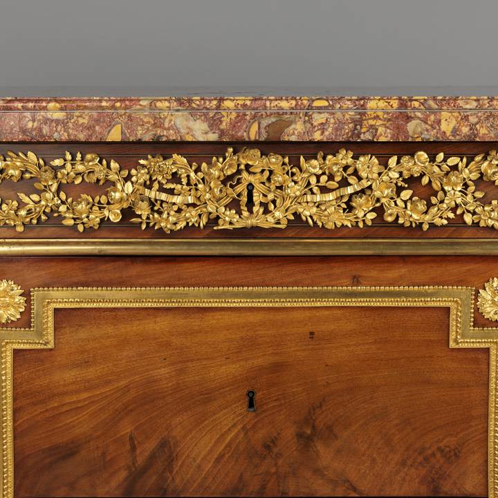 A detail of the gilt-bronze frieze mounts of a mahogany-veneered chest of drawers