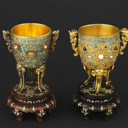 Two gold cups decorated with jewels and blue bird feathers on stands