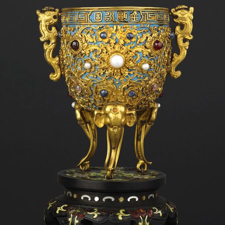 Gold cup decorated with jewels and blue bird feathers on stands