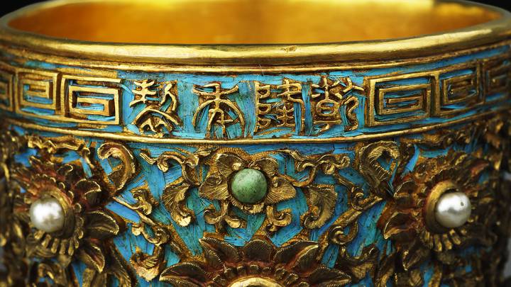 Detail of gold cup decorated with jewels and blue bird feathers
